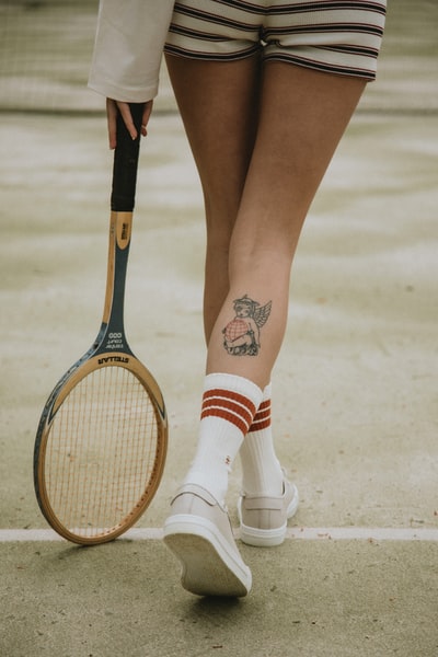 穿着白色和红色袜子和白色皮鞋，手持棕色和黑色网球拍的妇女